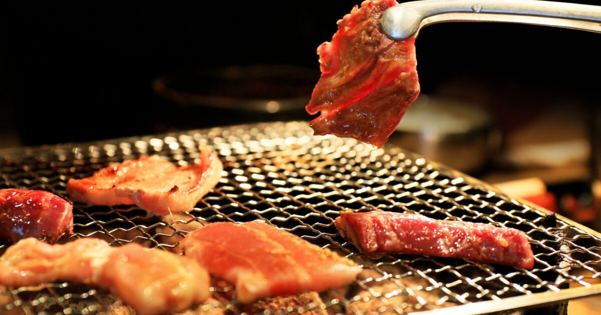 炭火網で焼かれる焼肉とトングを持つ手元