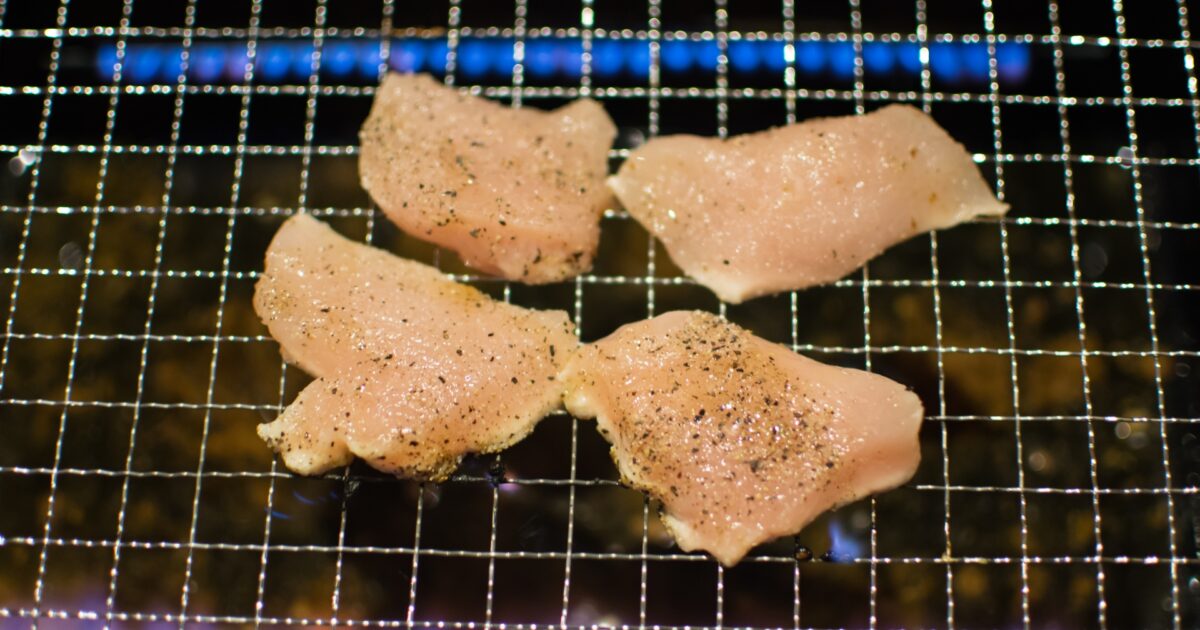 網の上で焼かれる塩胡椒を振った鶏むね肉の焼肉