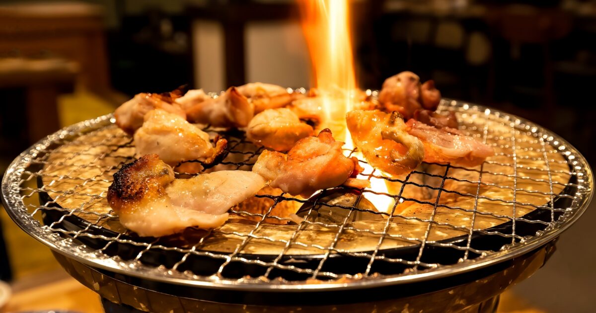 炭火で炎を上げながら焼かれる鶏もも肉の焼肉