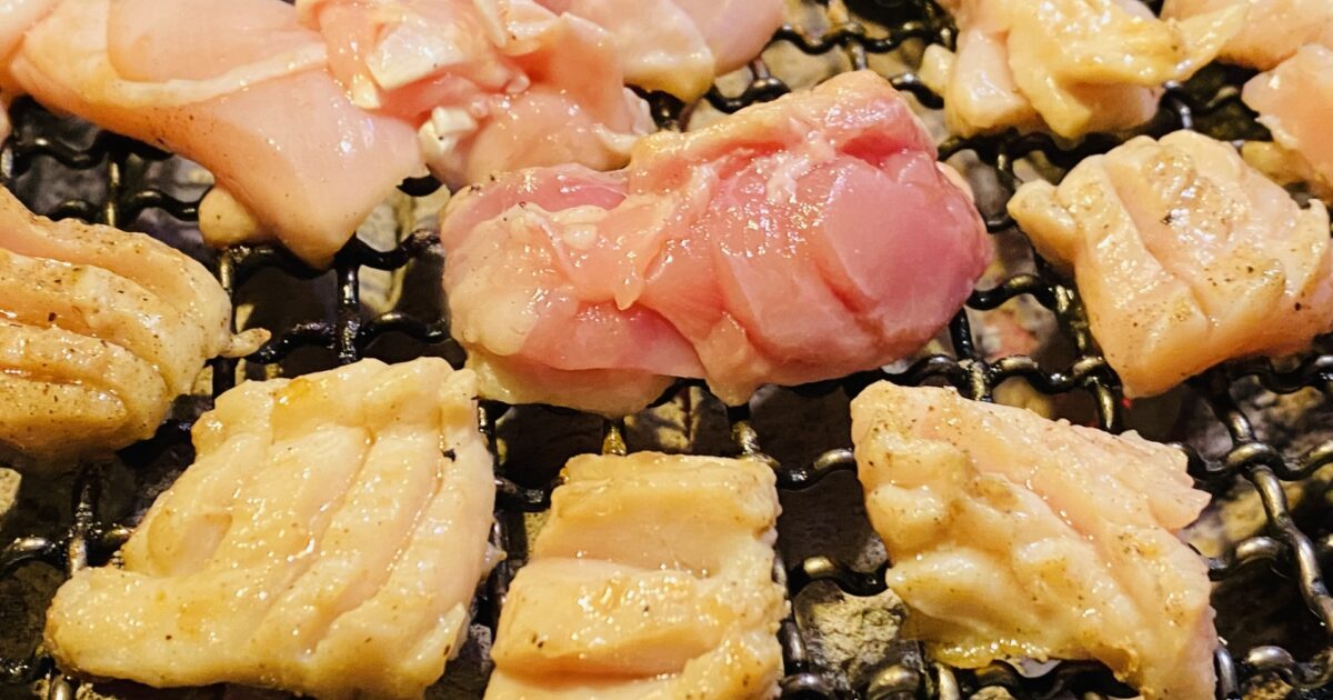 網の上で焼かれる複数の鶏もも肉と皮付き肉の焼肉