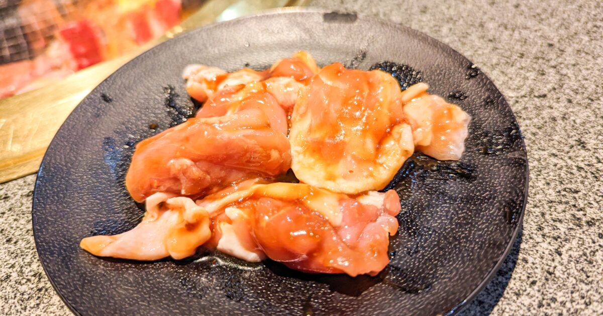 焼肉コンロの前に置かれたタレ漬け鶏肉の黒皿盛り