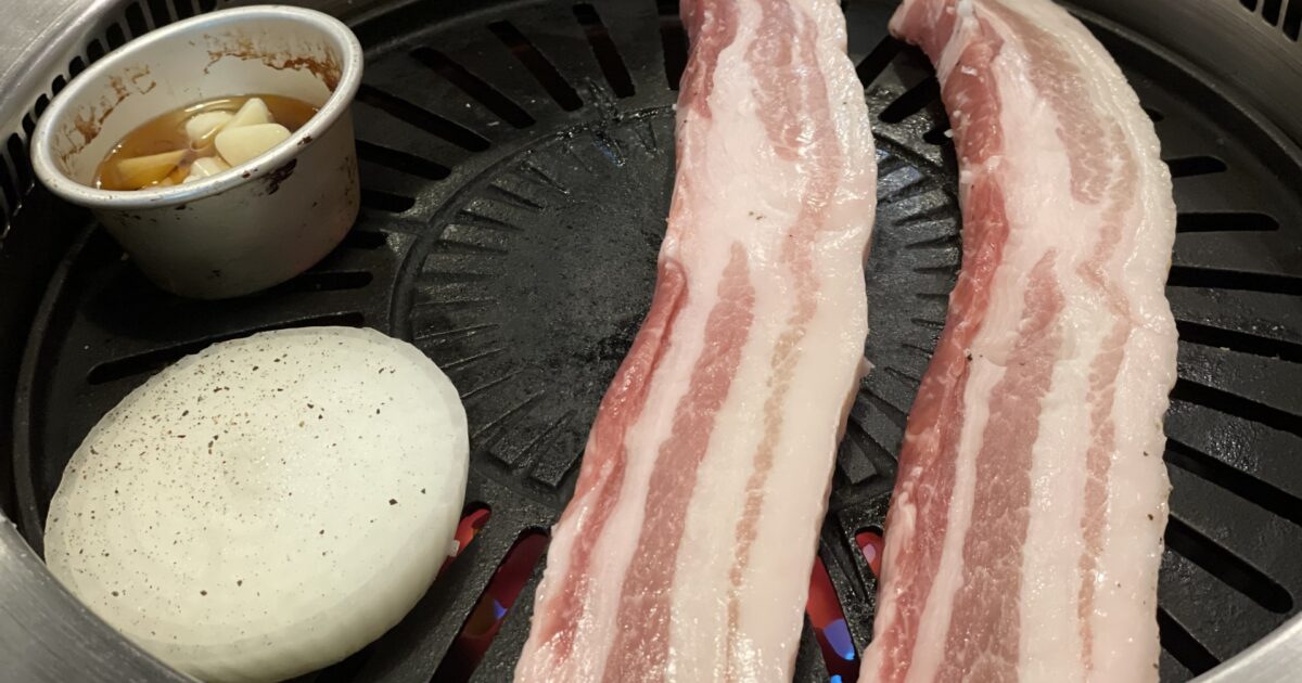 鉄板で焼かれる厚切り豚バラ肉と玉ねぎとにんにく