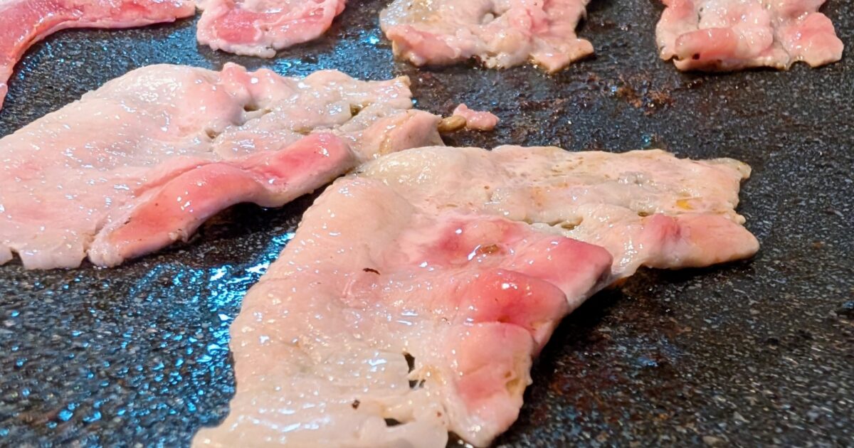 ホットプレートで焼かれる薄切り豚バラ肉の焼肉