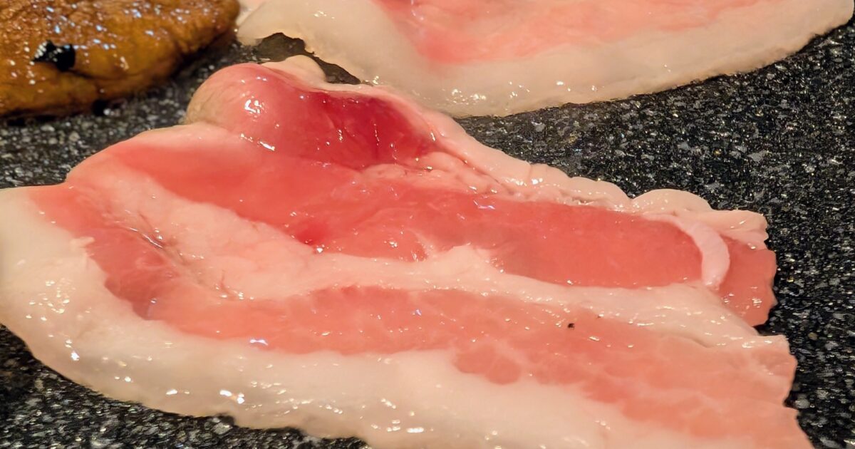 鉄板で焼かれる脂身の多い豚バラ肉のアップ