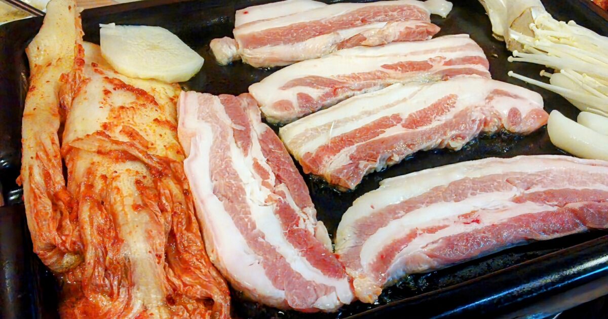 鉄板で焼かれる厚切り豚バラ肉とキムチときのこ
