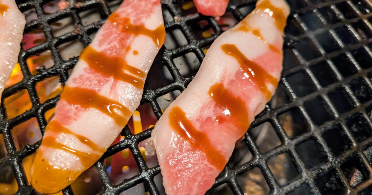 甘辛いタレがかかった豚バラ肉を網焼きで調理